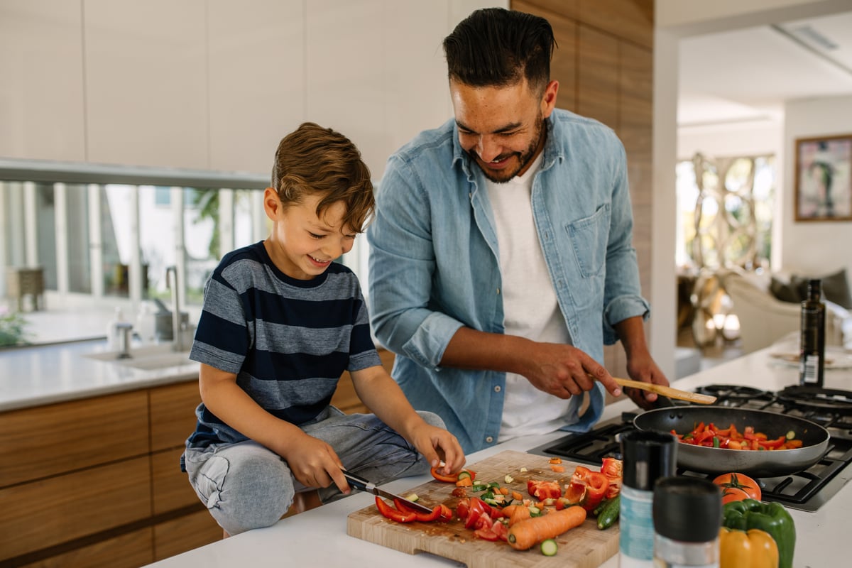 Small boy cooking with his father, both smiling