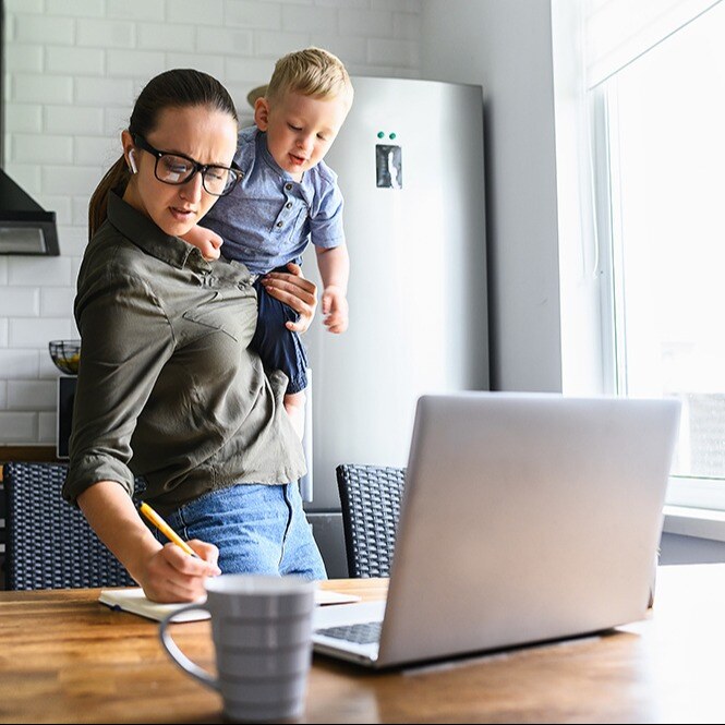 Busy young mom holding her child on her hip and she writes something down in a notebook