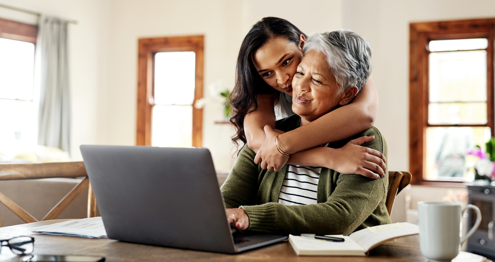 Latinx daughter hugging mother using laptop