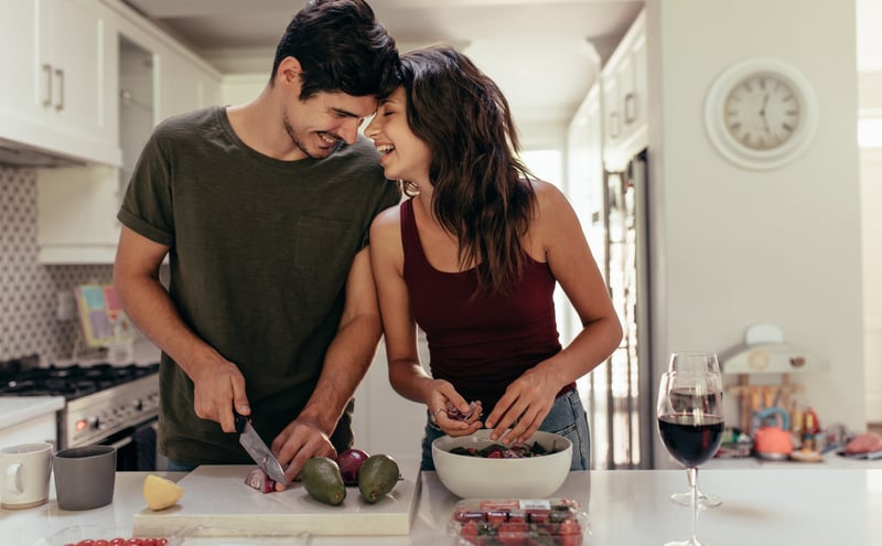 A young couple laughing and smiling as they prepare fruits and vegetables in the kitchen