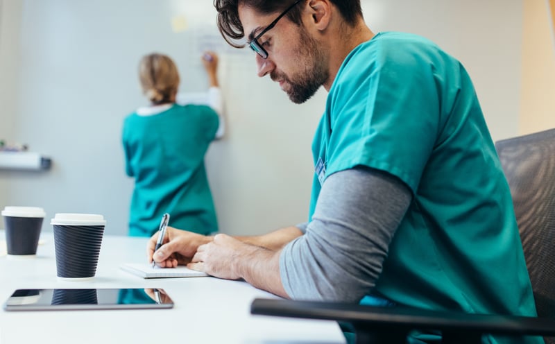 Young male nurse taking notes while looking at a tablet